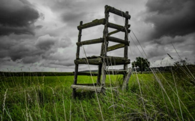 Picture of a field with a wooden stucture and gray clouds in the sky.